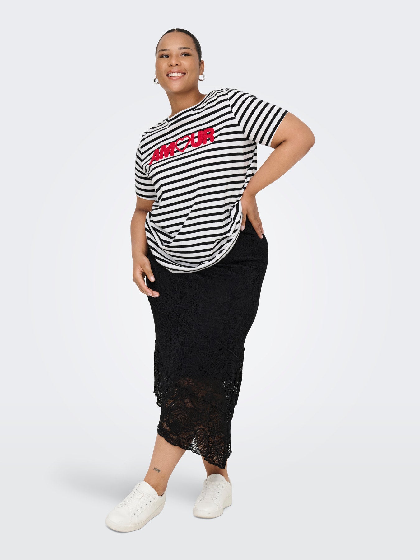 Femme grande taille portant un t-shirt marinière et une jupe en dentelle noire
