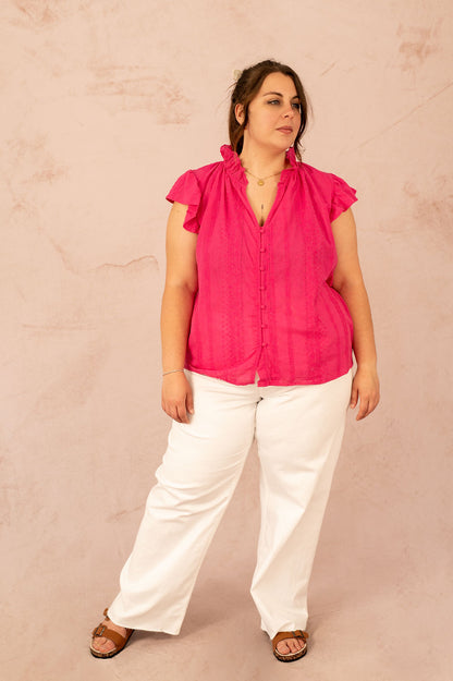 Femme portant la blouse Alizée rose fuchsia avec pantalon blanc, tenue grande taille estivale.
