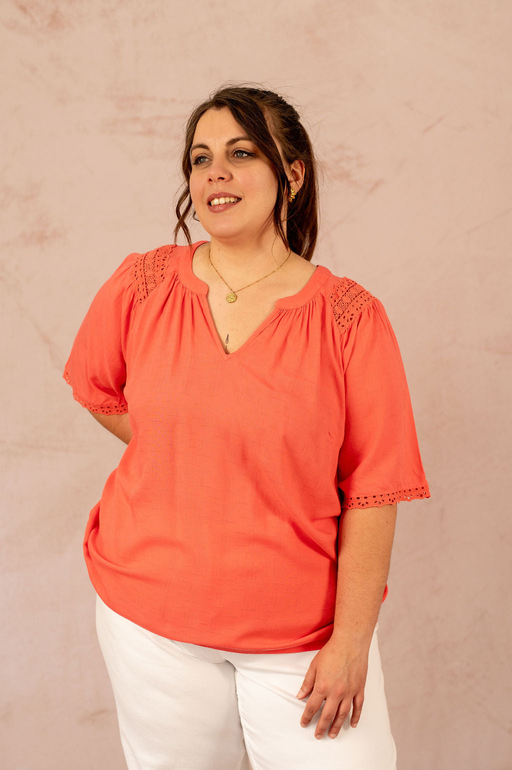 Portrait d'une femme souriante en blouse fluide corail à manches courtes ajourées