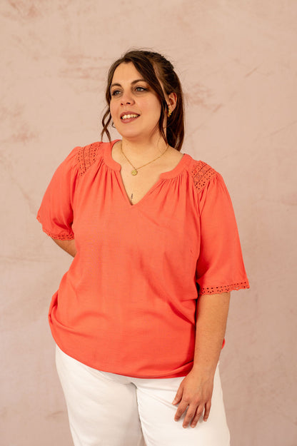 Portrait d'une femme souriante en blouse fluide corail à manches courtes ajourées