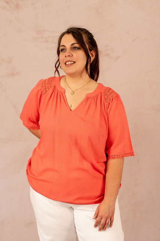Portrait d'une femme souriante en blouse fluide corail à manches courtes ajourées