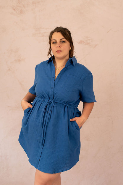 Femme portant la robe Abigail en gaze de coton bleu, vue de face avec mains dans les poches.
