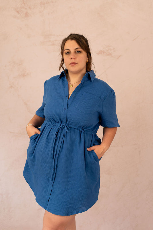 Femme portant la robe Abigail en gaze de coton bleu, vue de face avec mains dans les poches.
