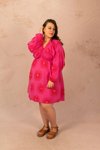 Femme portant une robe courte rose à imprimé soleil, manches longues et décolleté, mode grande taille Laïlla