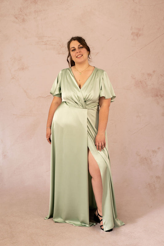 Femme portant une robe longue satinée vert sauge fendue à l'avant – Robe Luisa, collection cérémonie grande taille