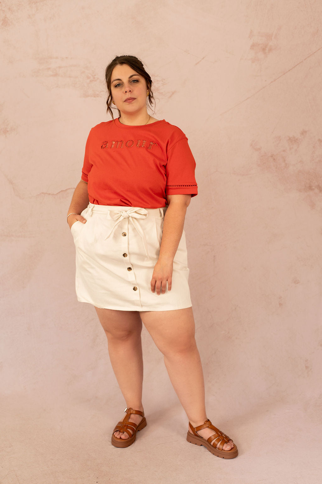 Femme plus size portant un t-shirt rouge "amour" et une jupe blanche boutonnée, look estival décontracté